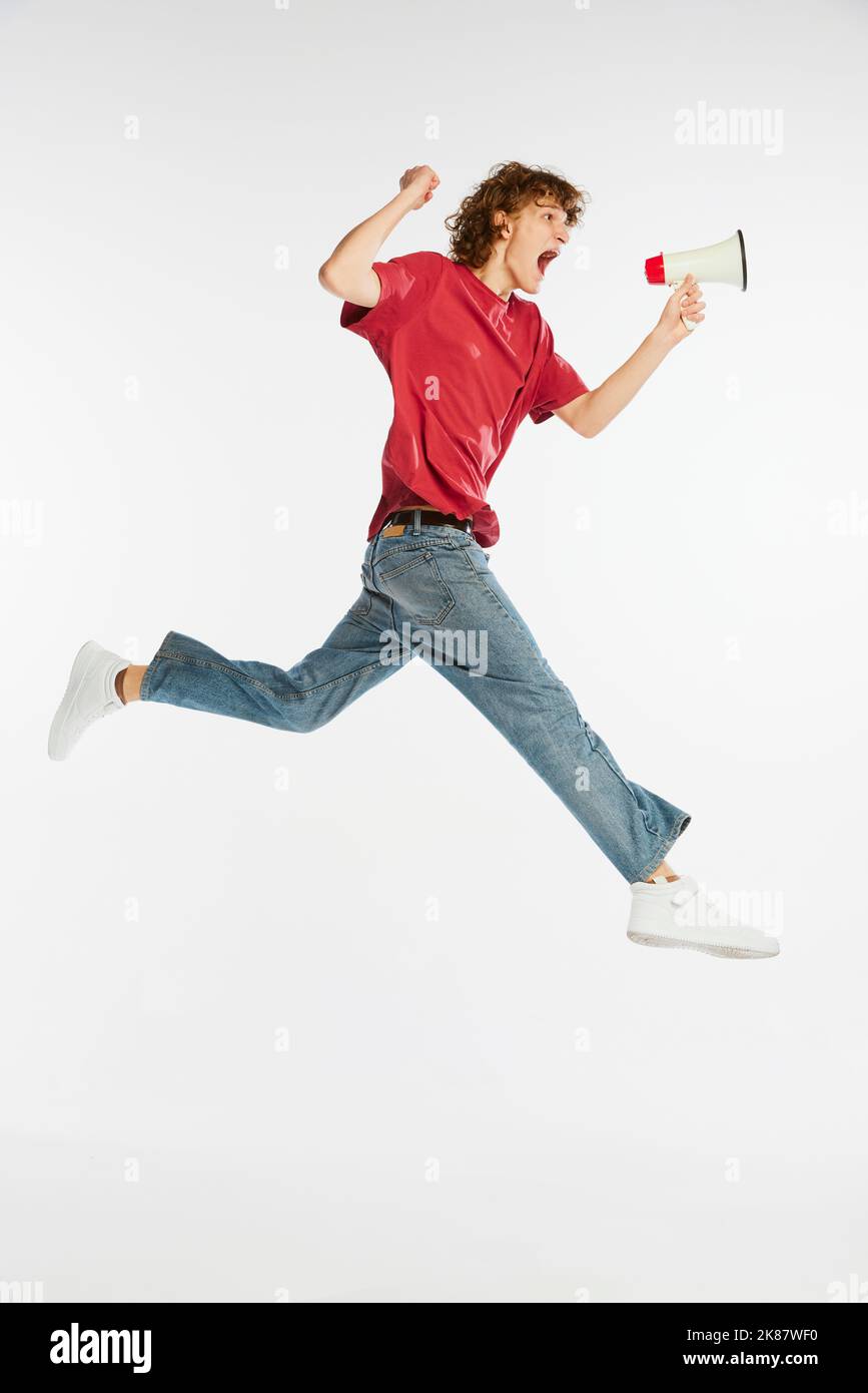 Un jeune homme ravie sautant et criant sur un haut-parleur isolé sur fond blanc. Nouvelles, sport, danse, fitness, bonheur Banque D'Images