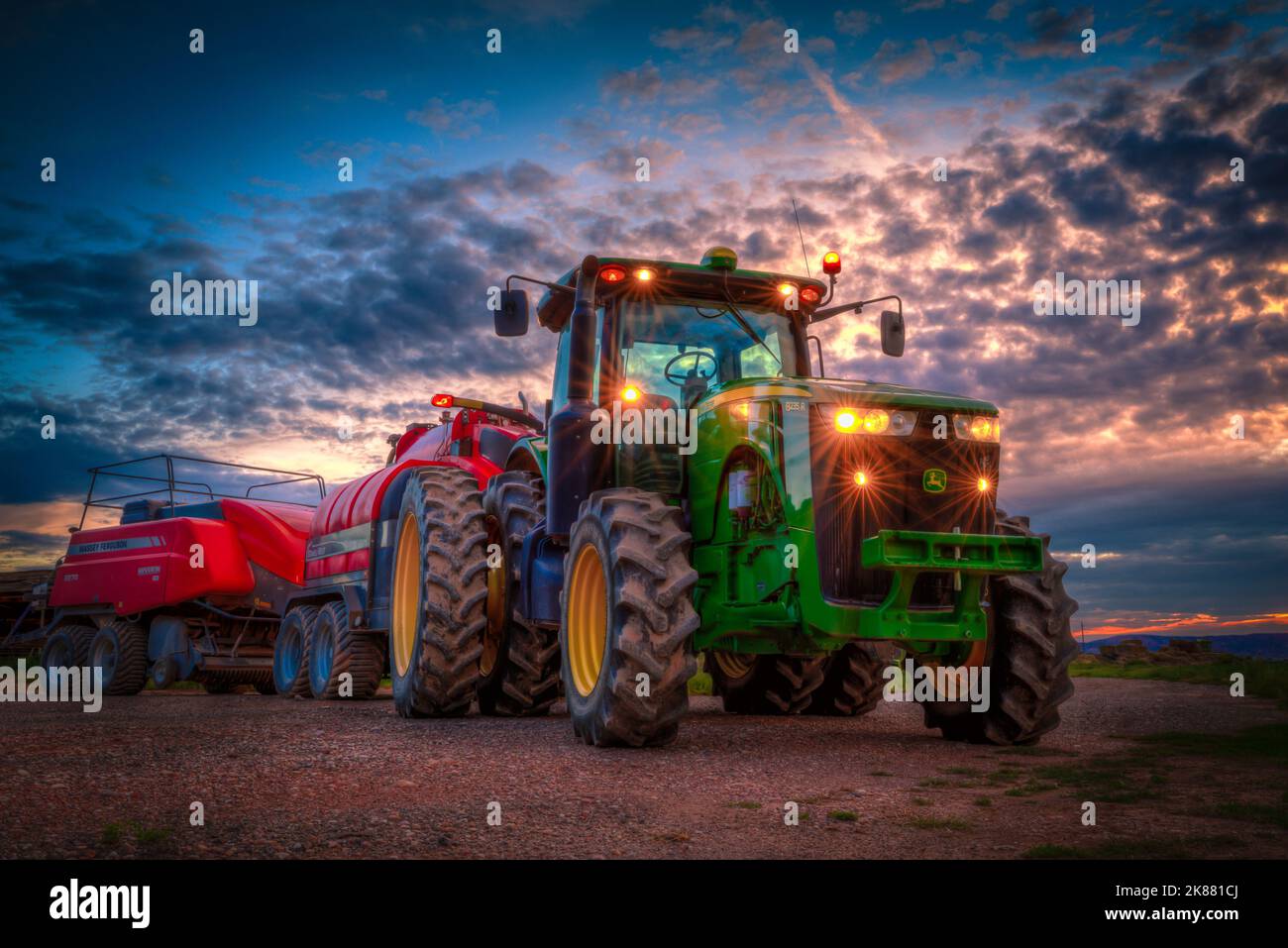 Un gros plan à faible angle d'un tracteur tirant le défroisseur et la presse à balles sur la ferme au coucher du soleil, à l'extérieur de Parowan, Utah Banque D'Images