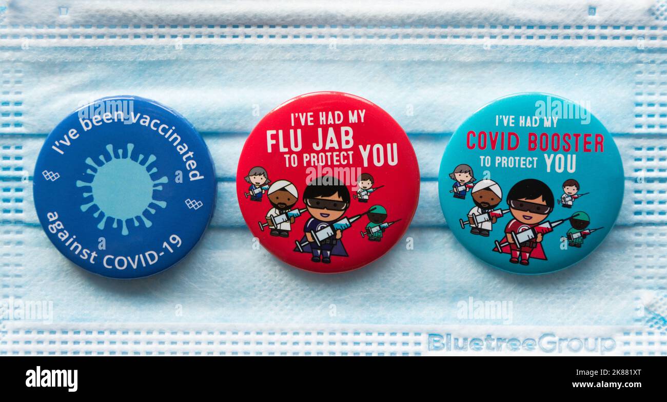 Badges colorés Covid 19 Booster et Flu Jab reposant sur un masque chirurgical Banque D'Images