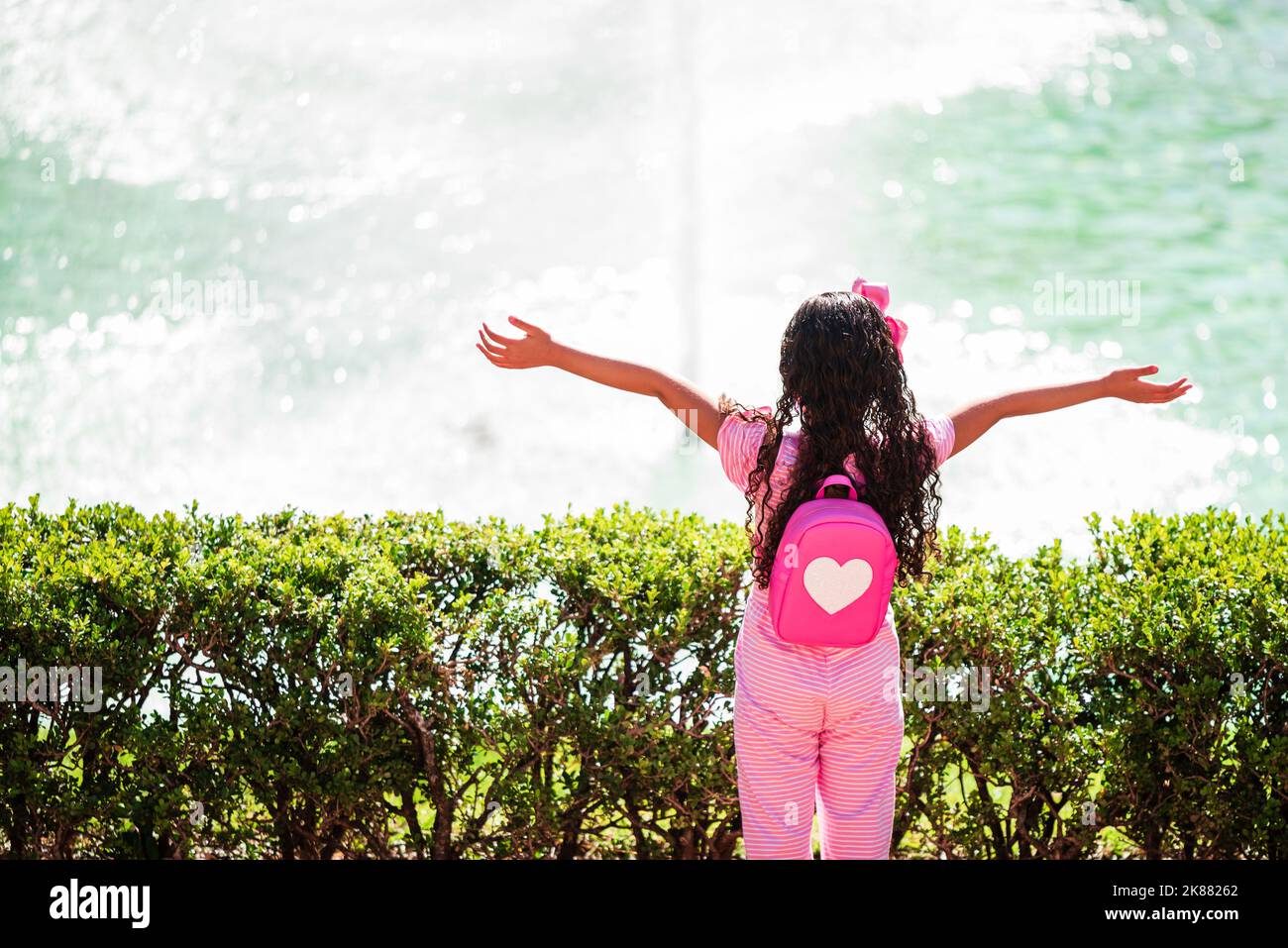 Vue arrière d'une fille brésilienne regardant la fontaine à Praça da Liberdade à Belo Horizonte avec bras ouverts et coeur sur sac à dos rose. Banque D'Images