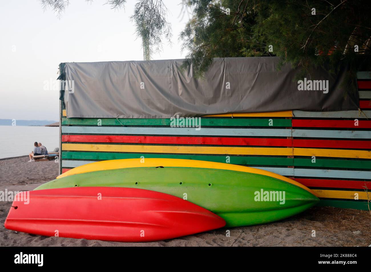 Kayaks / canoës et hangar coloré sur une plage de sable, Lesbos. Septembre / octobre 2022. Automne. Deux personnes assises. Banque D'Images