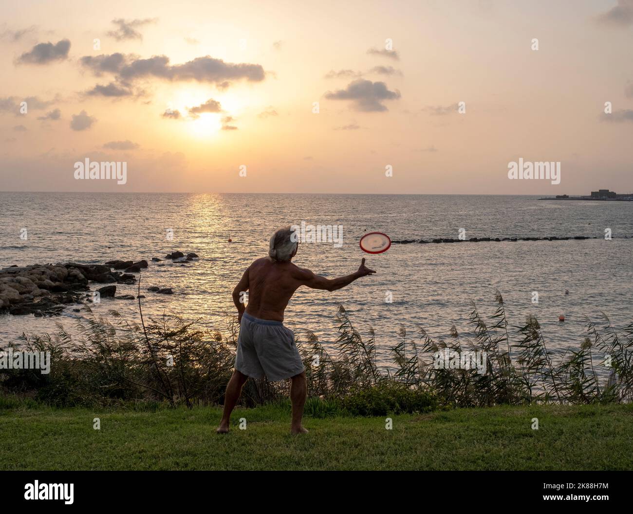 Un homme s'exerçant sur une plage qui jette une Frisbee, Paphos, Chypre. Banque D'Images