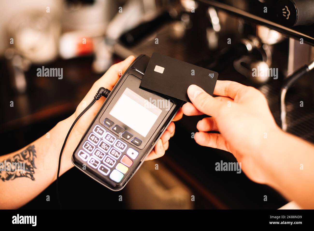 Le barista tient le terminal du lecteur de carte de crédit pendant que le client effectue un paiement sans contact à l'aide d'une carte de crédit Banque D'Images