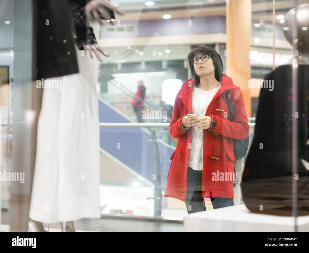 Une femme se fait une place sur des mannequins dans un magasin de vêtements. Tenue décontractée suspendue aux mannequins. Vue via la fenêtre transparente de la boutique. Shopping au centre commercial. Vêtements de base Banque D'Images