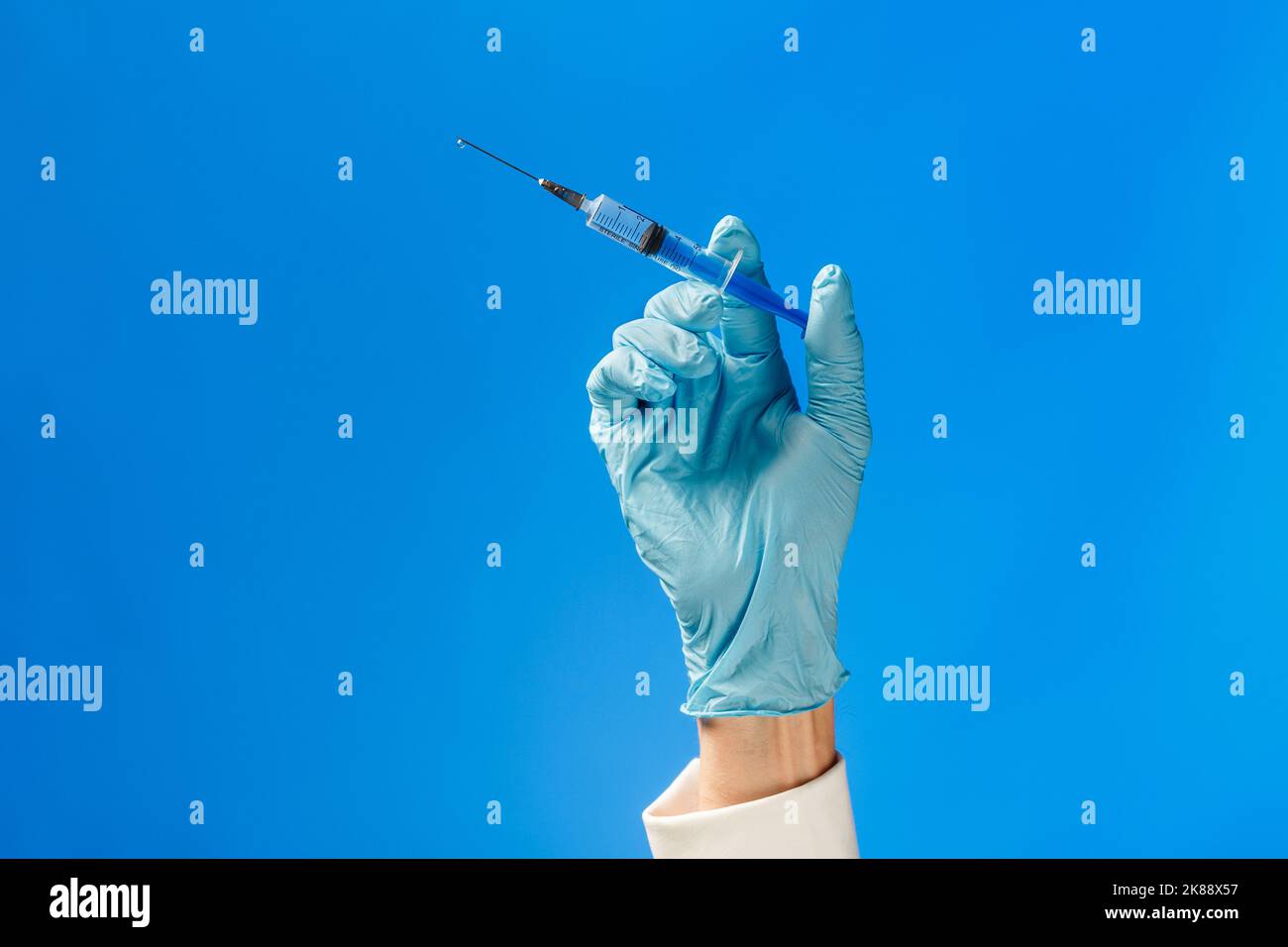 Main dans un gant en caoutchouc bleu tenant une seringue sur fond bleu. Concept d'injection médicale. Banque D'Images