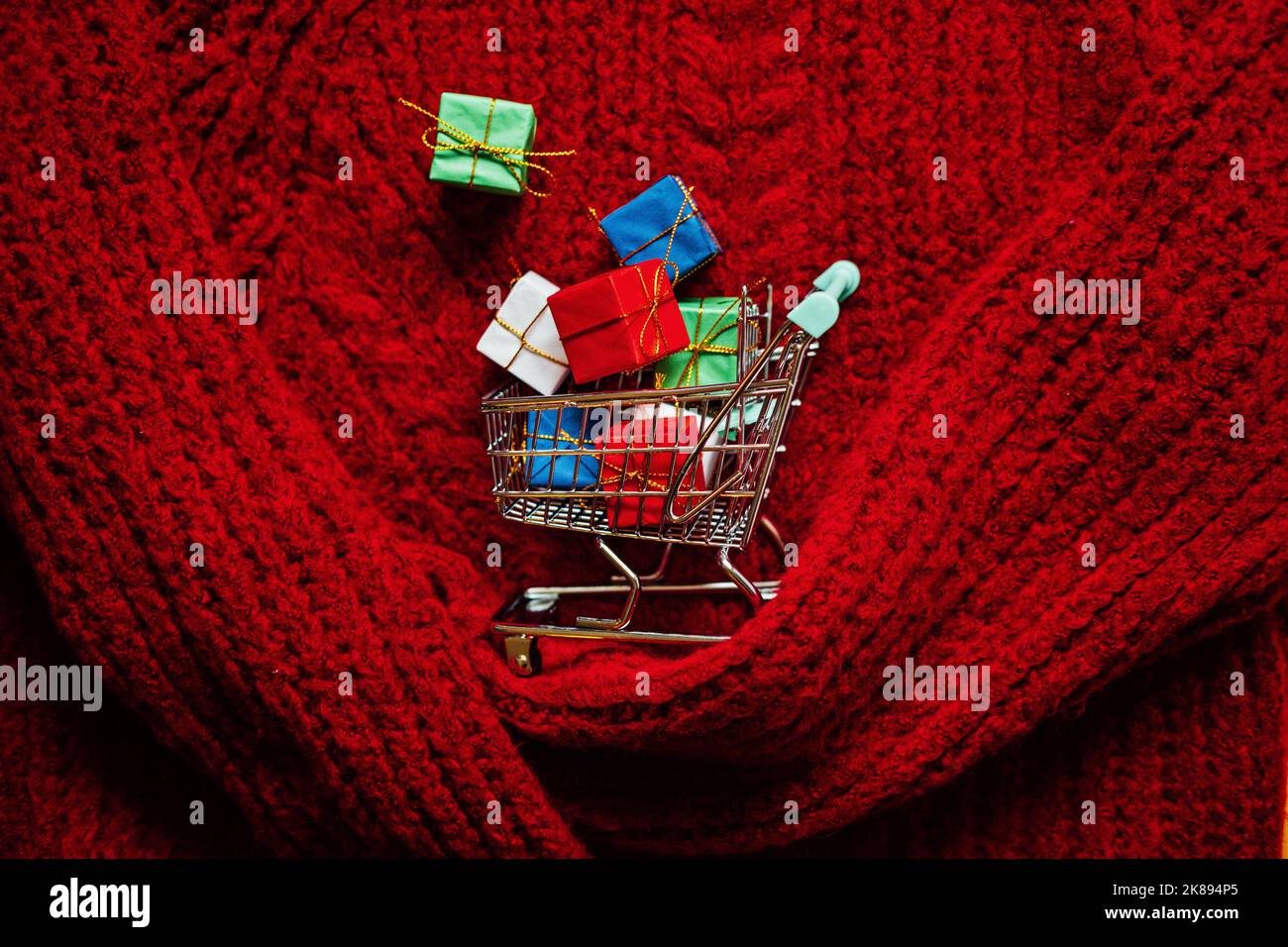 Noël concept de vente anticipée. Panier avec de nombreuses boîtes-cadeaux sur fond de tricot rouge Banque D'Images