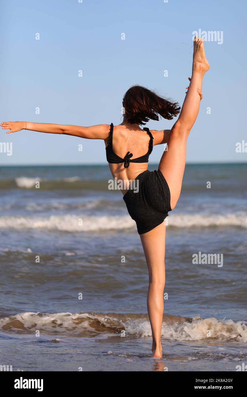 jeune fille pieds nus en maillot de bain noir des exercices de gymnastique rythmique sur la mer Banque D'Images