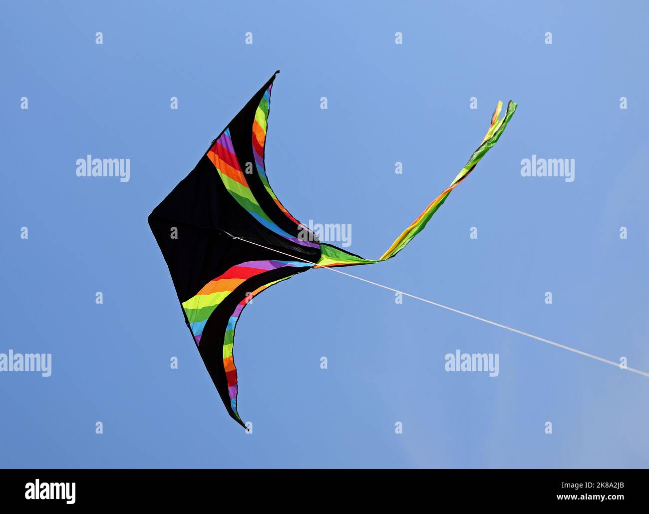 CERF-volant NOIR avec des bandes de différentes couleurs de l'arc-en-ciel volant sur le ciel bleu Banque D'Images