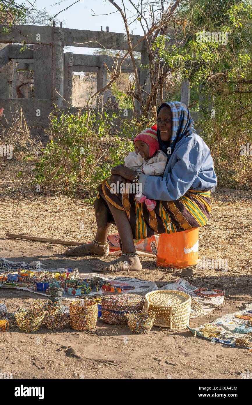 Tarangire, Tanzanie - 12 octobre 2022:Une femme Masai tenant un bébé tout en vendant des bijoux faits main et des ornements sur un bord de route à l'aube. Banque D'Images