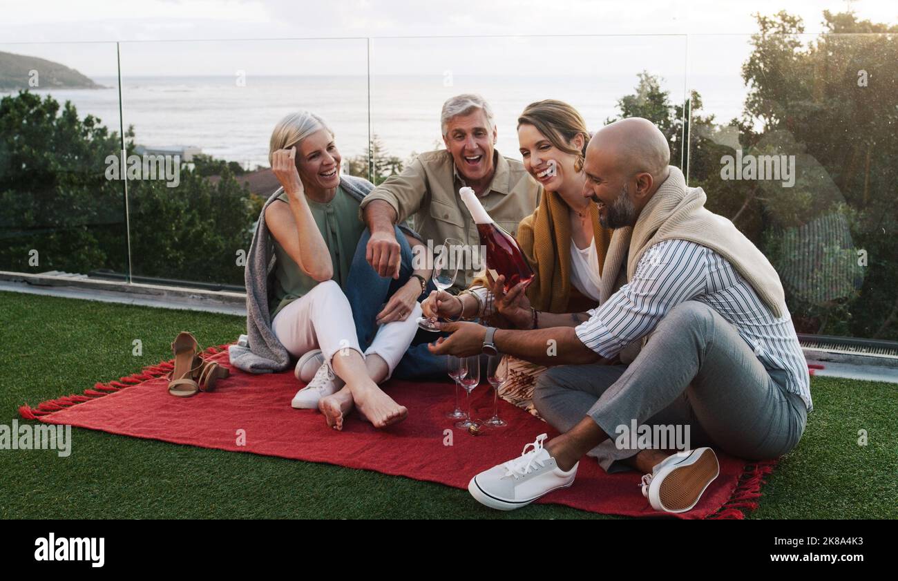 Ouvrez le pétillant, faites-vous sourire. Deux couples heureux assis ensemble et pique-niquer dehors tout en buvant du champagne. Banque D'Images