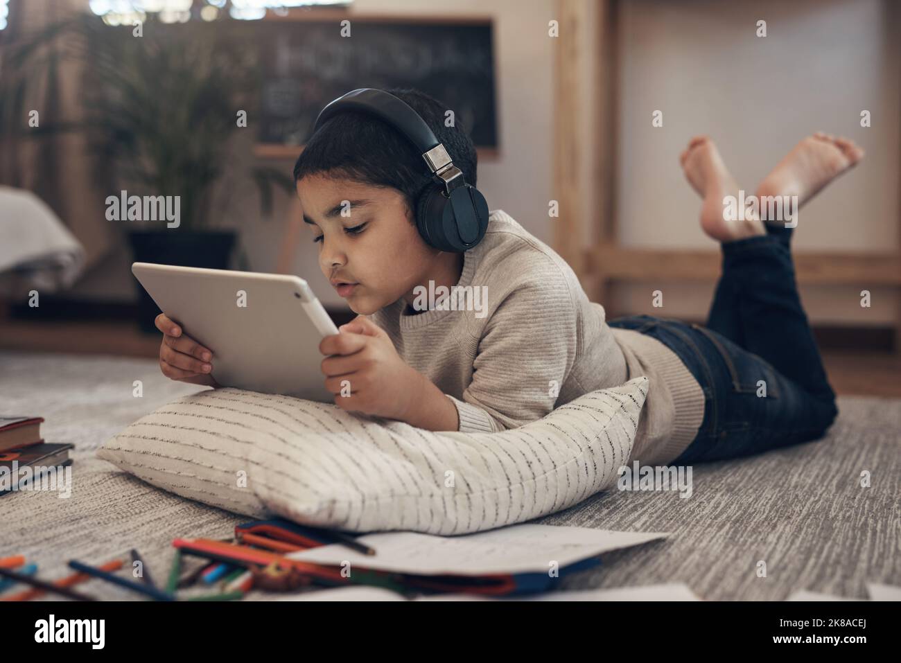 Un petit garçon adorable qui utilise une tablette et un casque numériques tout en effectuant une mission scolaire à Banque D'Images