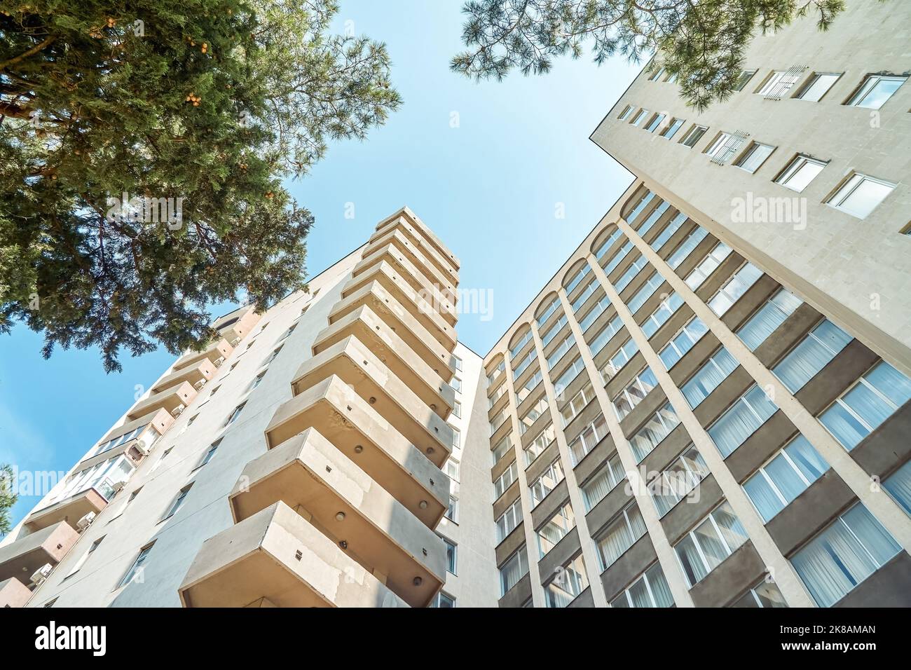 Ancien bâtiment urbain de haute élévation soviétique avec balcons et fenêtres voûtées contre de végétation luxuriante et ciel clair par jour ensoleillé dans la ville vue à angle bas. Banque D'Images