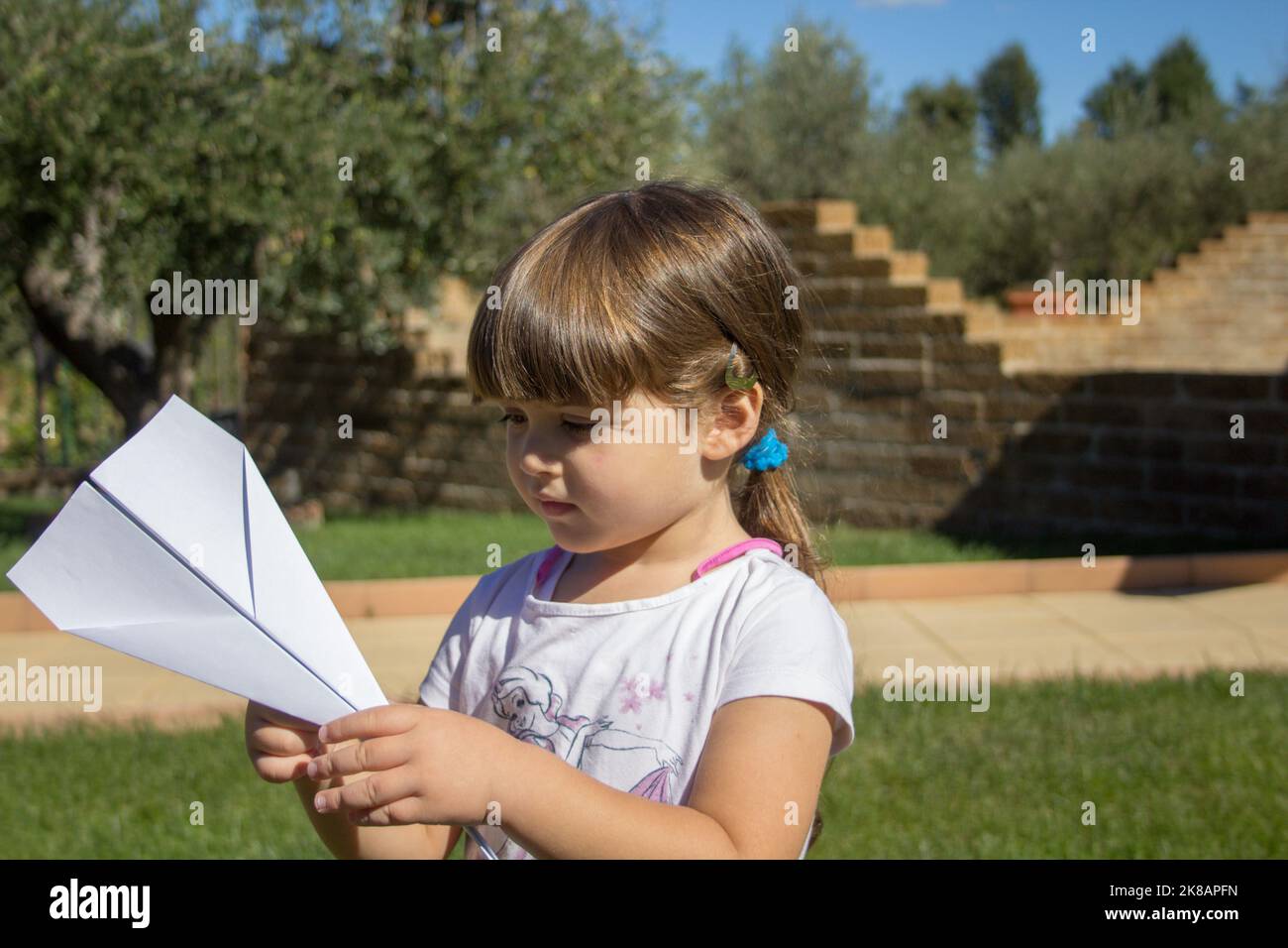 Photo d'une adorable petite fille jouant un petit avion de papier volant dans l'arrière-cour. Jeux pour enfants en plein air Banque D'Images
