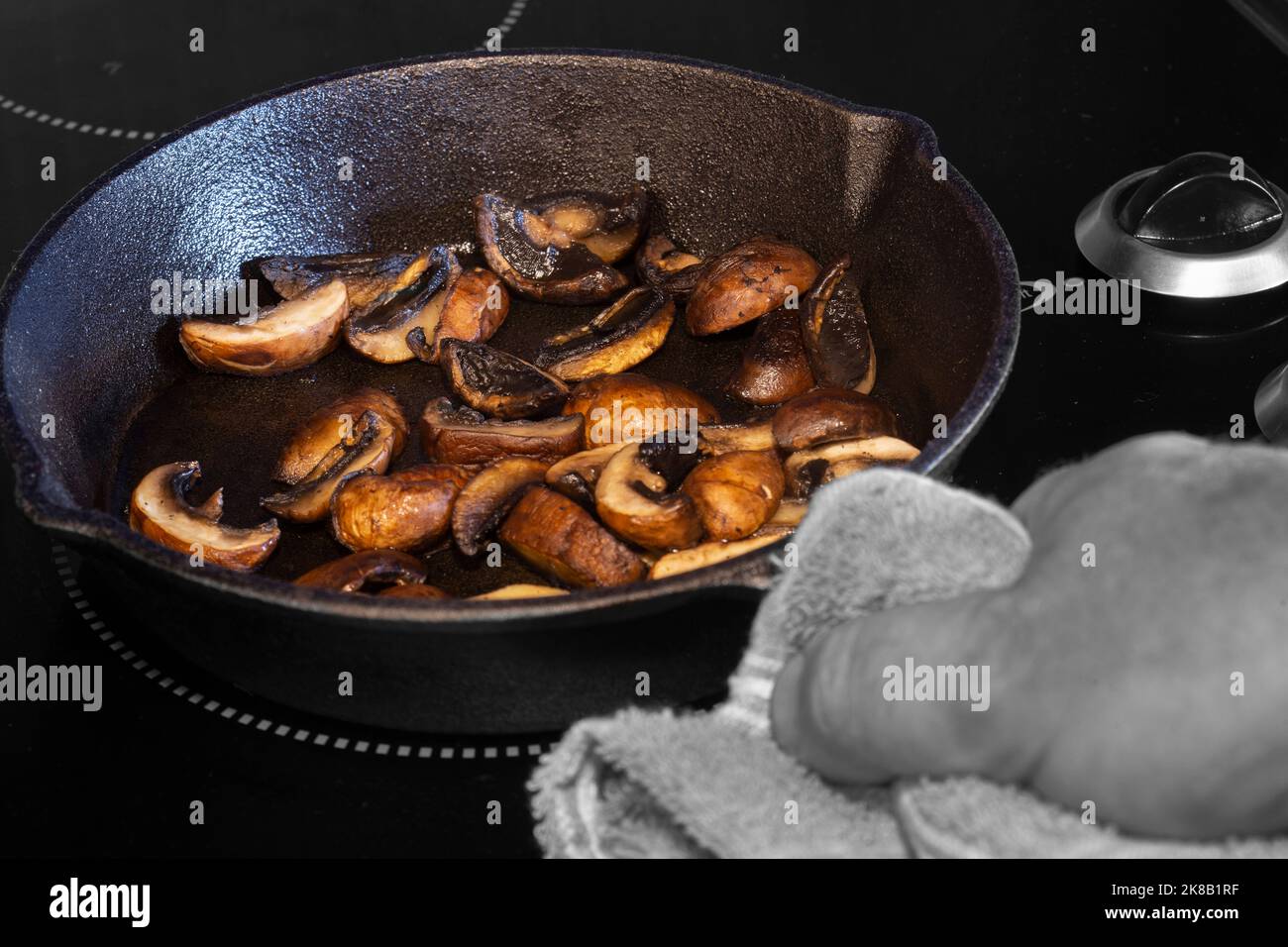 Friture de champignons châtaigniers, avec un homme tenant une poêle en fonte avec une torchon, sur une cuisinière électrique Banque D'Images