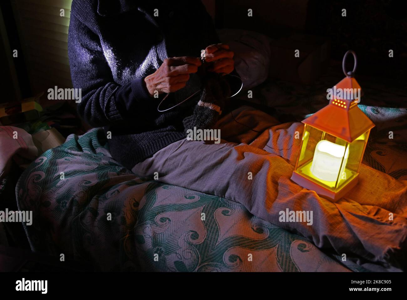 Une femme ukrainienne frappe des chaussettes pour des soldats ukrainiens à la lumière d'une lanterne électrique. Panne de courant - les missiles russes ont détruit des entreprises énergétiques Banque D'Images