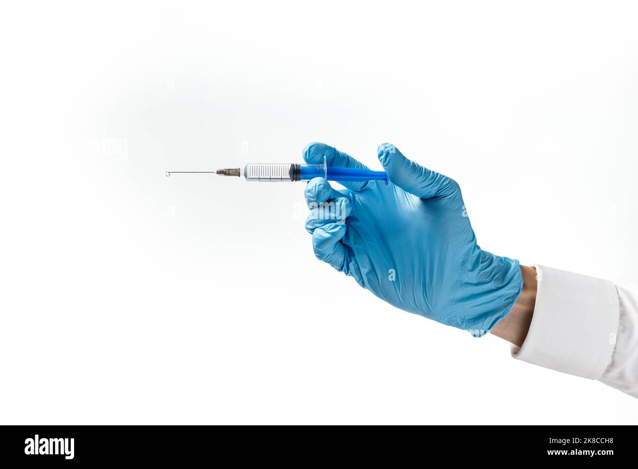 Seringue avec une goutte sur une aiguille à la main dans un gant en caoutchouc bleu sur fond blanc. Concept d'injection médicale. Banque D'Images