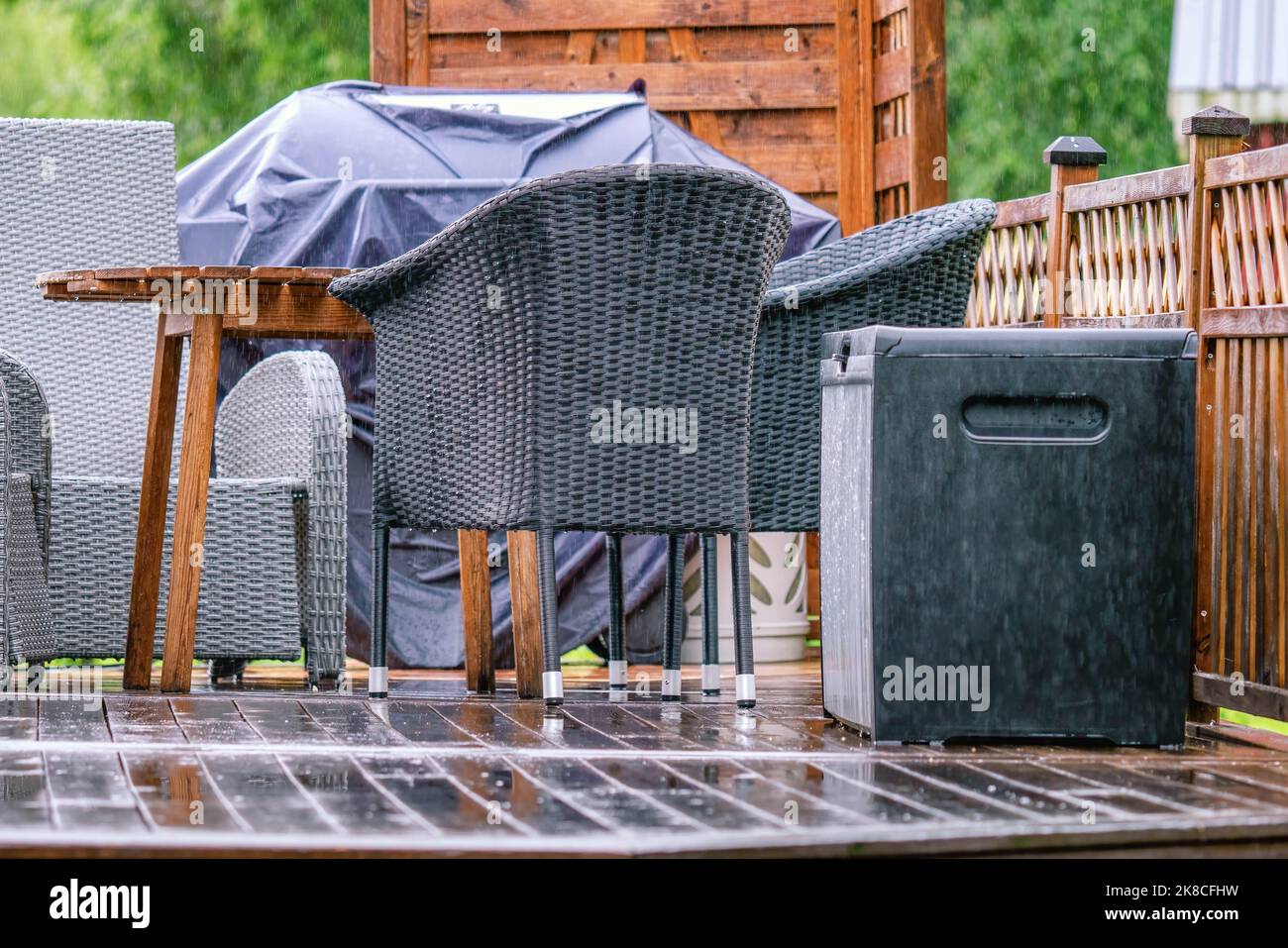 Forte pluie sur terrasse en bois avec chaises d'été, table en bois, grill couvert de pluie. Forêt verte floue en arrière-plan. Tout est très nous Banque D'Images