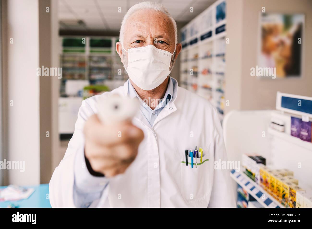 Un ancien pharmacien mesurant la température à l'aide d'un thermomètre sans contact à la pharmacie. Banque D'Images