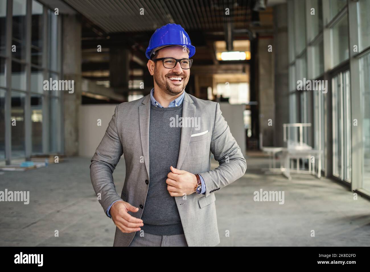 Homme d'affaires souriant avec casque debout dans le bâtiment en cours de construction et de vérification des travaux. Banque D'Images