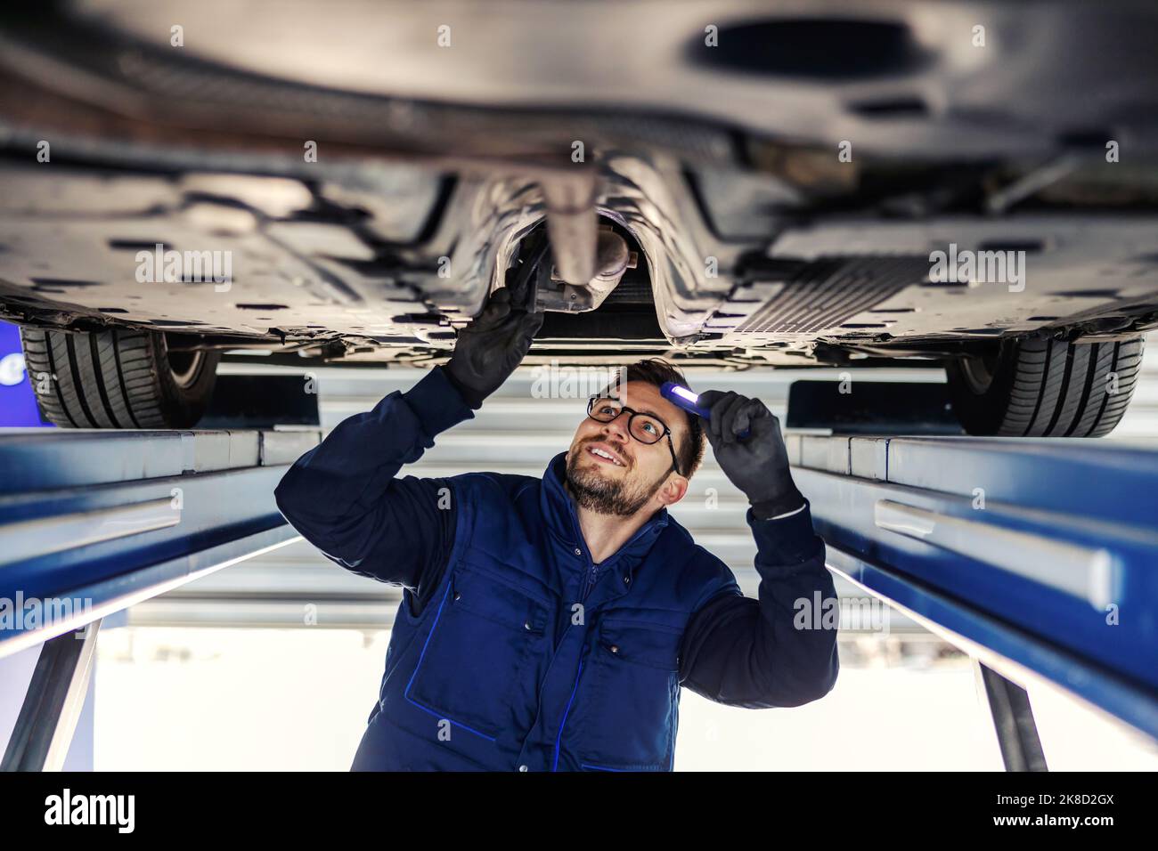 Inspection technique de la voiture. Service voiture en atelier. Un homme en uniforme bleu se tient sous une voiture dans le garage et contrôle les essieux de la voiture. Il Banque D'Images