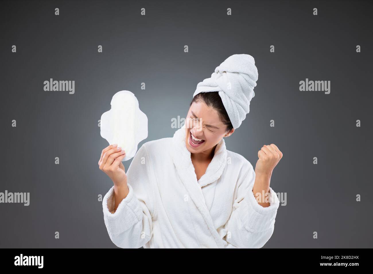 Protection pendant les règles. Une femme dans un peignoir et une serviette enveloppée autour de sa tête est heureuse d'avoir des articles prêts pour la menstruation. Elle tient une fée Banque D'Images
