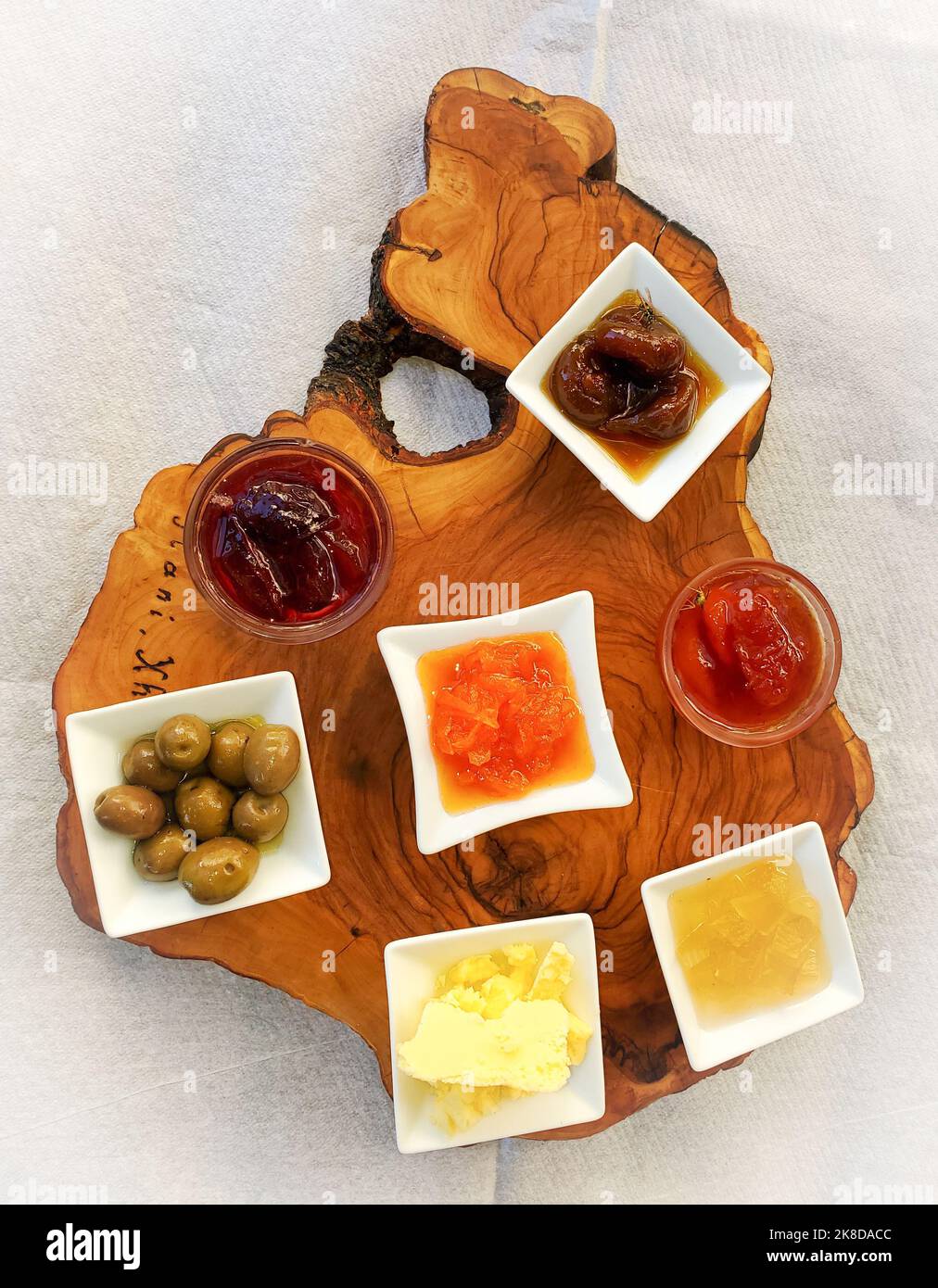 Plateau de service en bois avec sept petits plats de condiments avec olives vertes, beurre, coing, abricot et compote de prune ou confiture. Photographié fro Banque D'Images