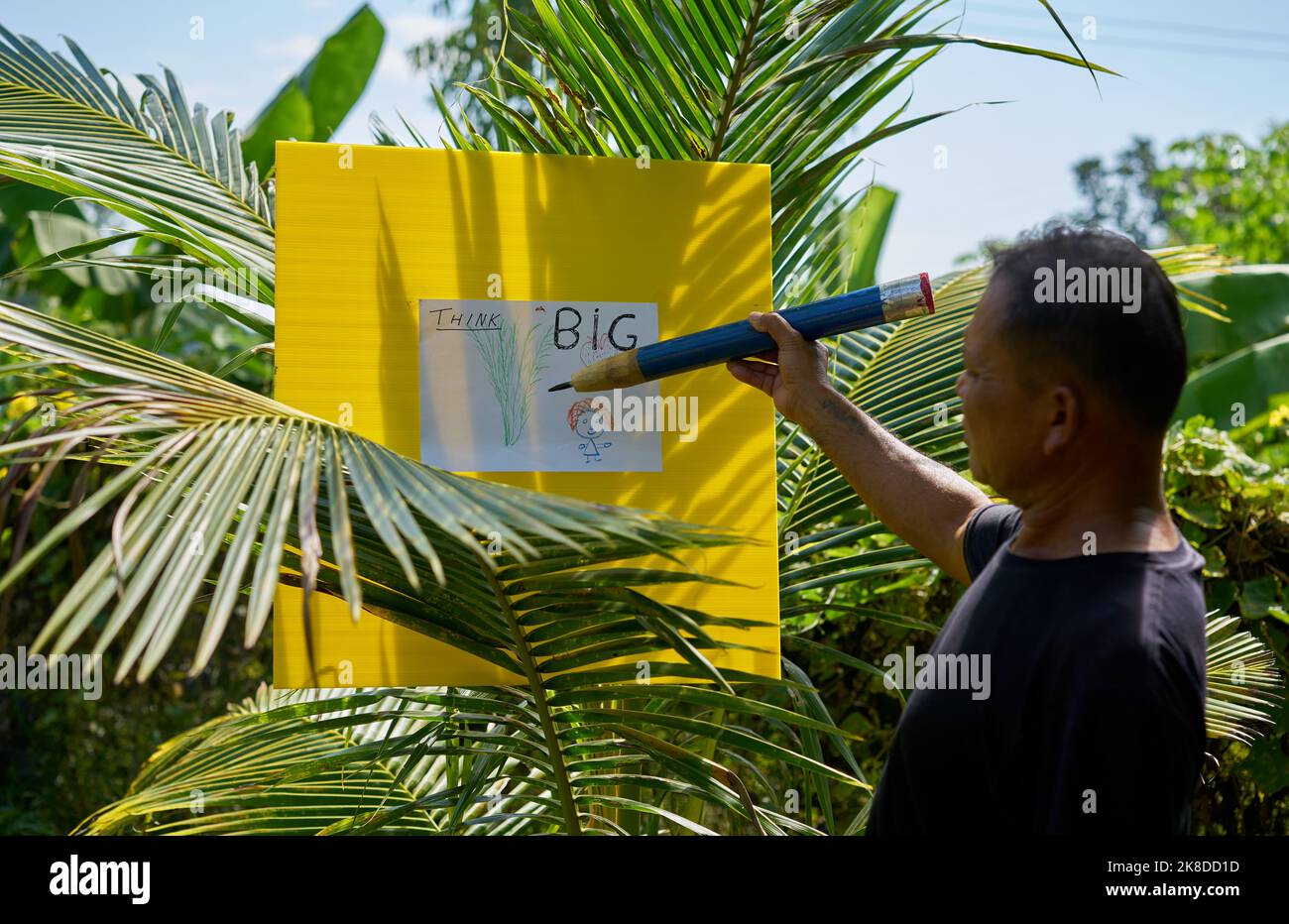 Un artiste dessine dans un jardin tropical à l'aide d'un très grand crayon. Banque D'Images