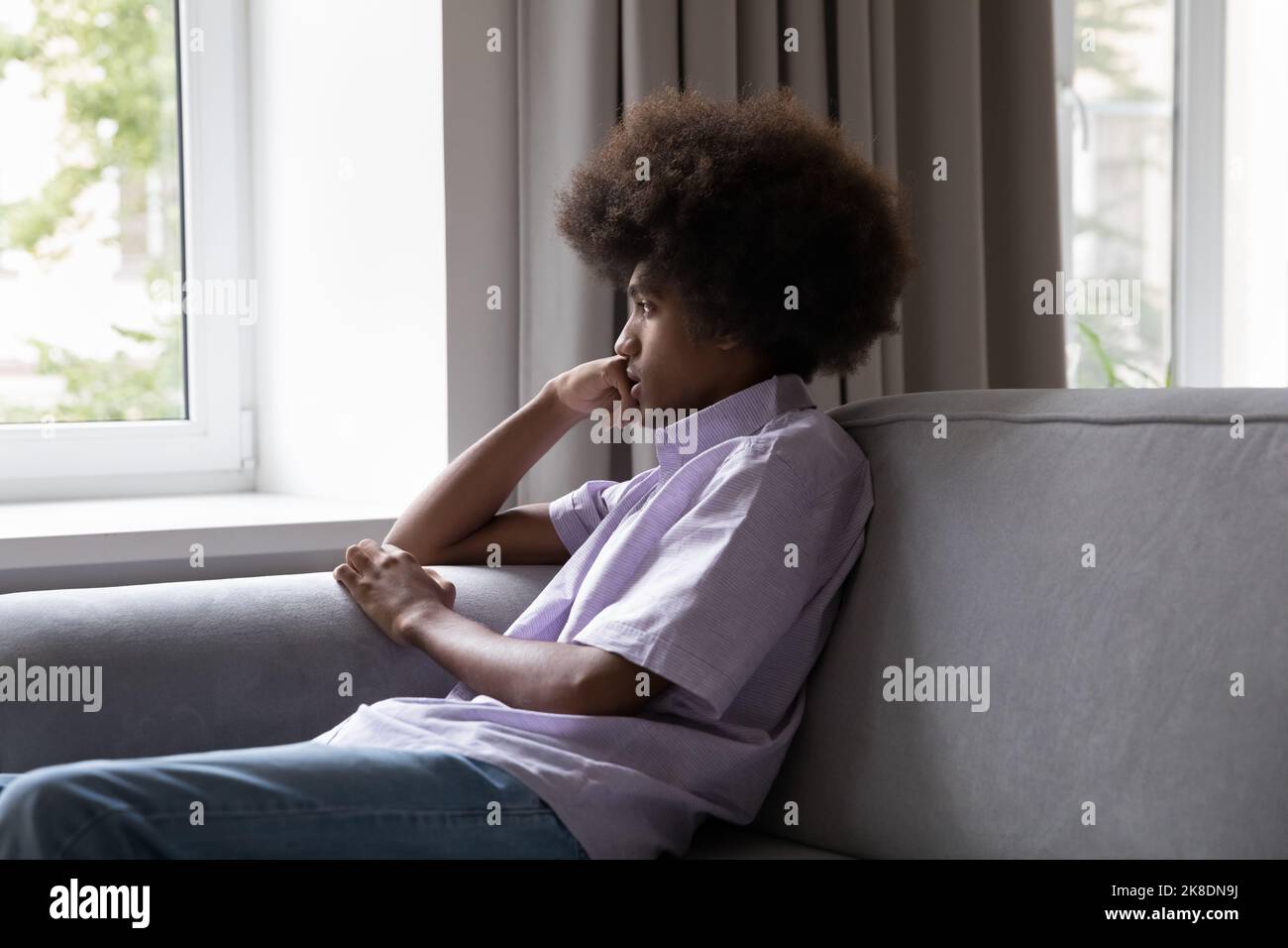 Un adolescent africain triste est assis sur un canapé donnant par la fenêtre Banque D'Images
