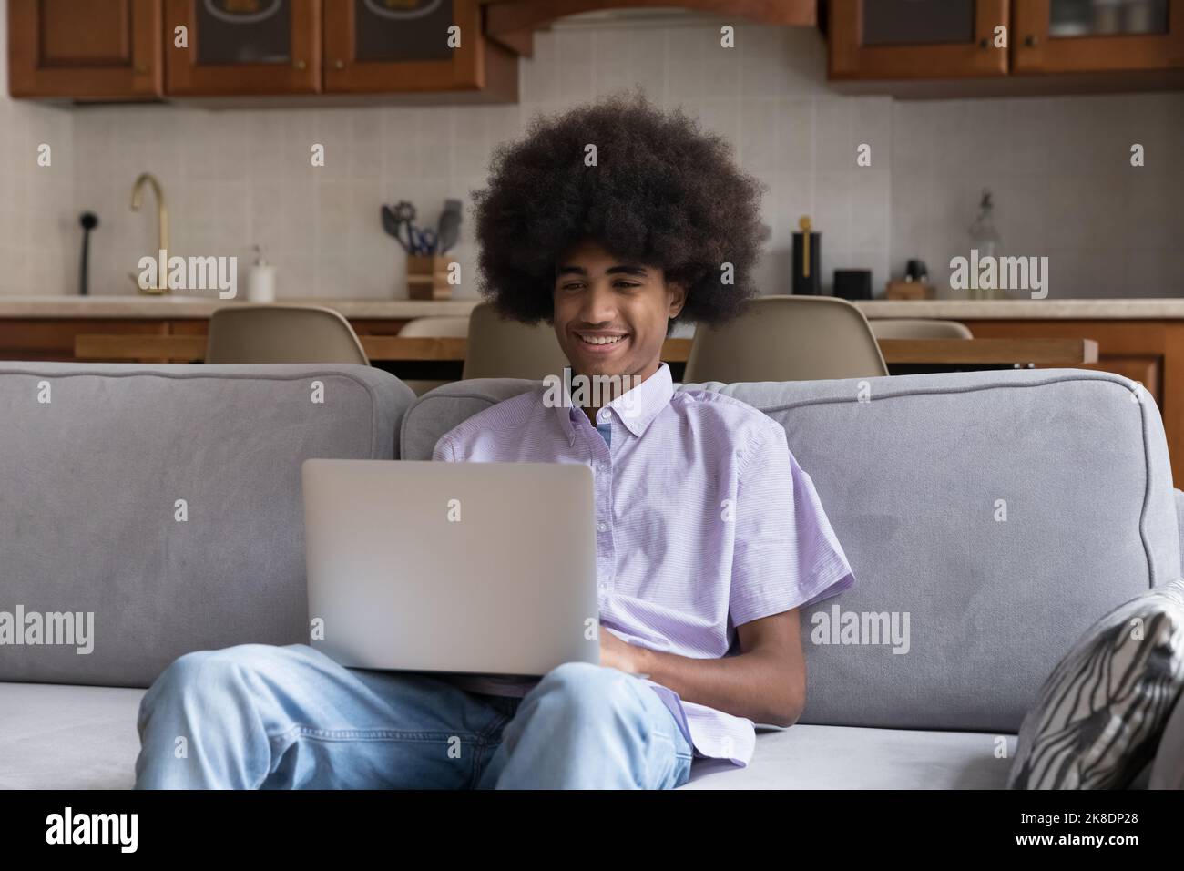 Un jeune garçon souriant s'assoit sur un canapé avec un ordinateur portable Banque D'Images