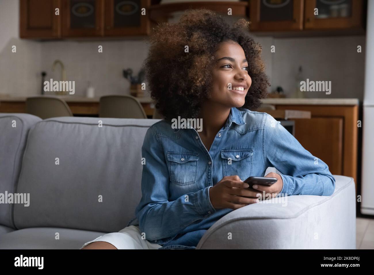 Belle adolescente africaine reposant sur un canapé avec un smartphone Banque D'Images
