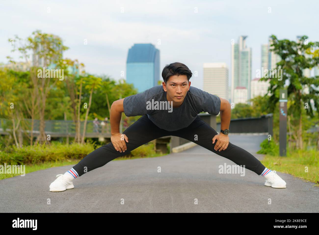 Sports urbains - un jeune homme asiatique se réchauffe avant de courir en ville pendant une belle journée d'été Banque D'Images