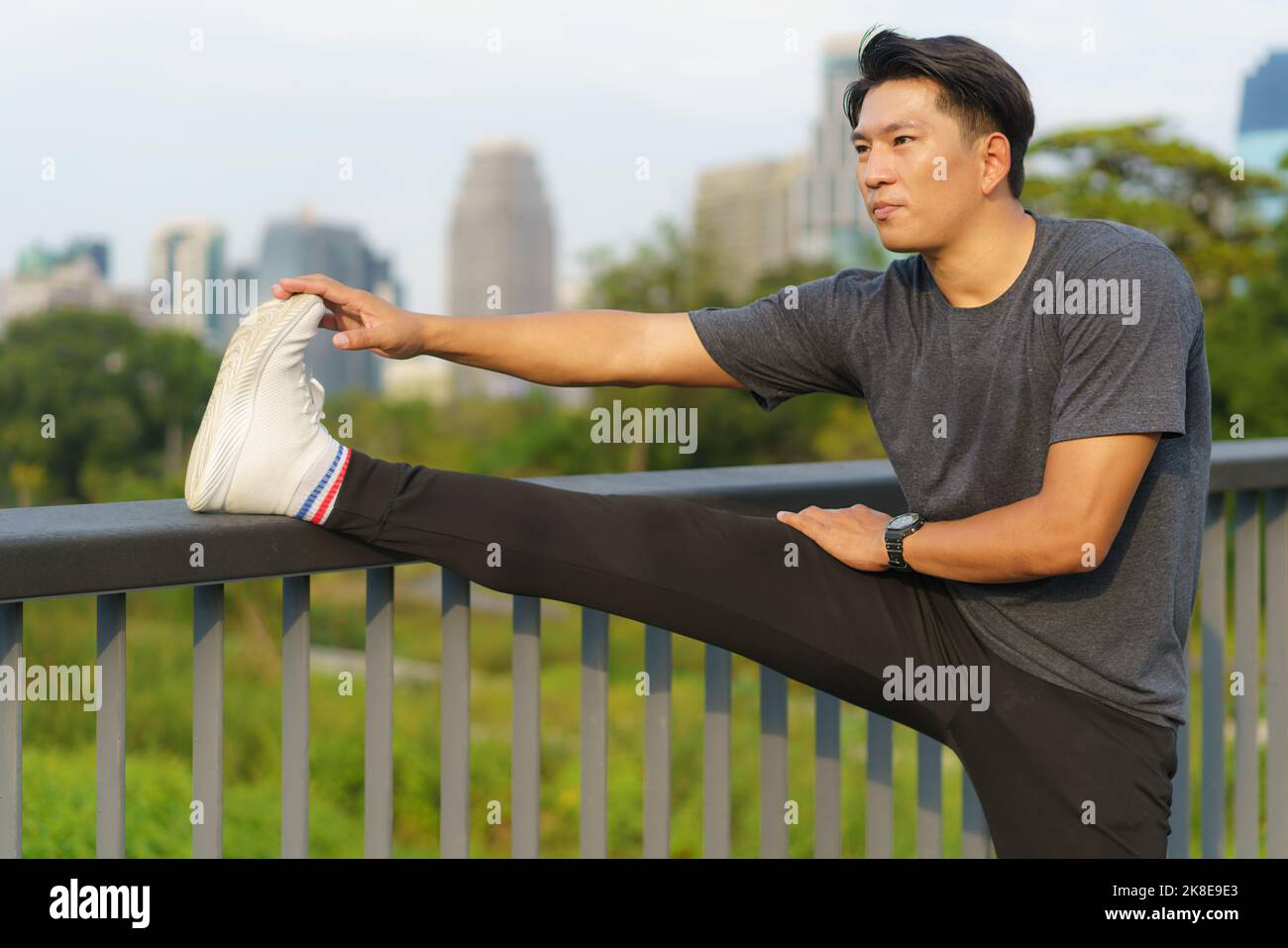 Sports urbains - un jeune homme asiatique se réchauffe avant de courir en ville pendant une belle journée d'été Banque D'Images