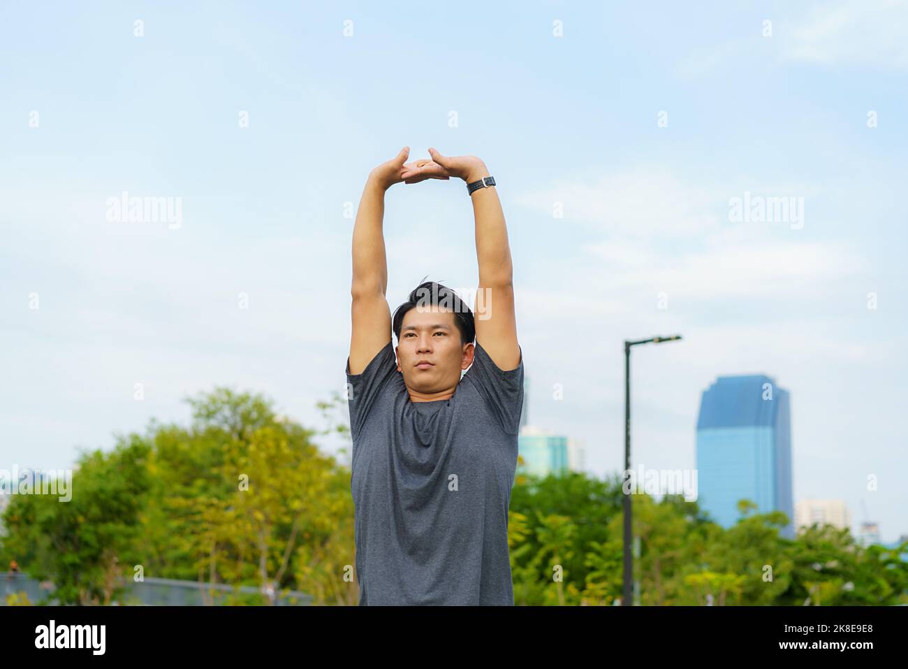 Sports urbains - un jeune homme asiatique se réchauffe avant de courir en ville pendant une belle journée d'été Banque D'Images