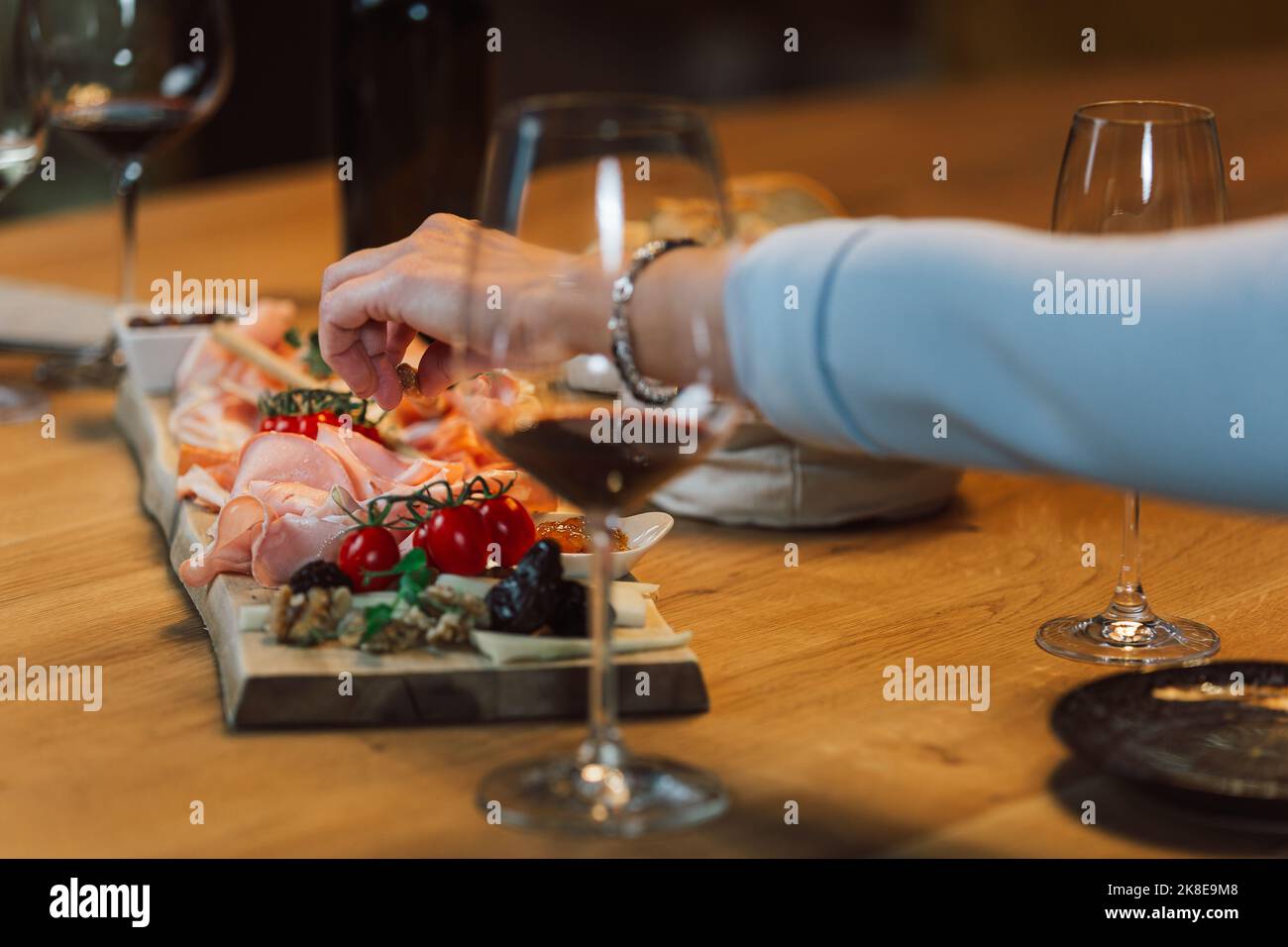 Main femelle prenant une amande d'un plat en bois avec prosciutto, fromage, pruneaux, noix et tomates cerises servi en accompagnement, gros plan. Banque D'Images