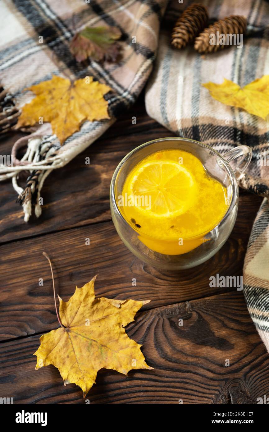 Concept d'automne saisonnier avec boisson. Tasse de thé chaud ​​​​buckthorn de mer avec citron, écharpe chaude et feuilles d'érable sur fond rustique. Banque D'Images