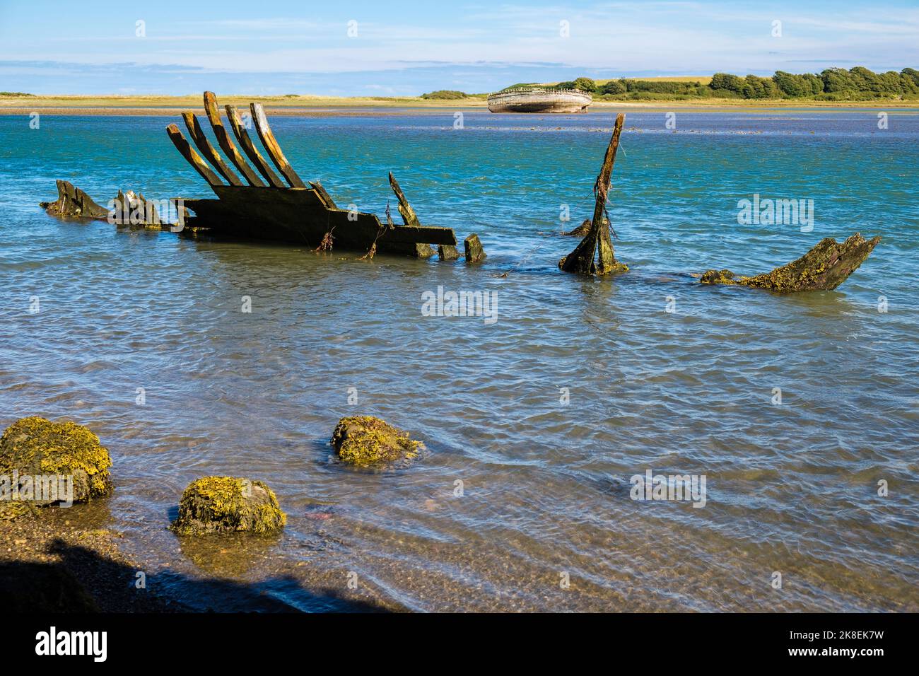 Restes d'une ancienne coque en bois d'une épave de navire avec une coque plus complète à travers la baie. Traeth Ducas, île d'Anglesey, pays de Galles du Nord, Royaume-Uni, Grande-Bretagne Banque D'Images