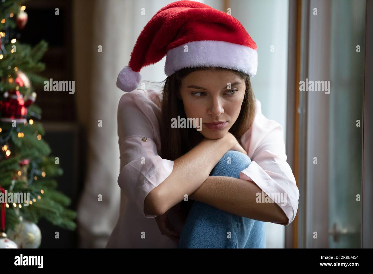 Jeune femme déprimé assise sur le rebord de la fenêtre, se sentant seule pendant les vacances. Banque D'Images