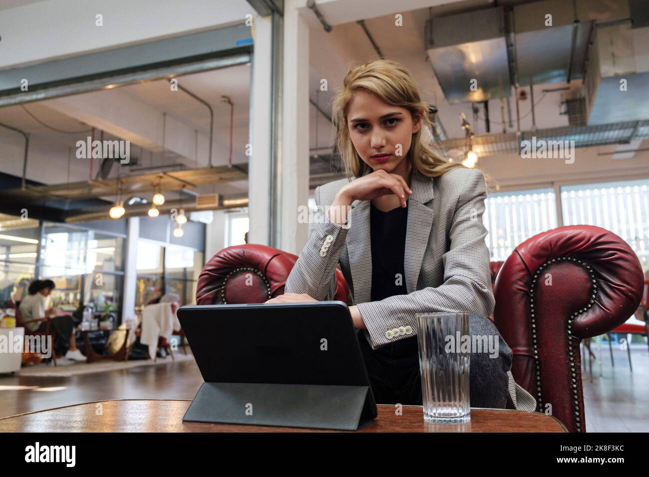 Jeune femme assise dans un fauteuil travaillant sur une tablette numérique Banque D'Images