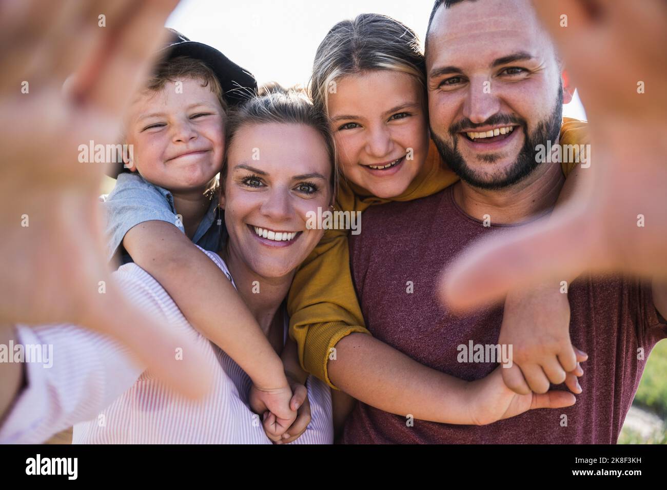 Rire la famille embrassant et regardant à travers les mains l'appareil photo Banque D'Images