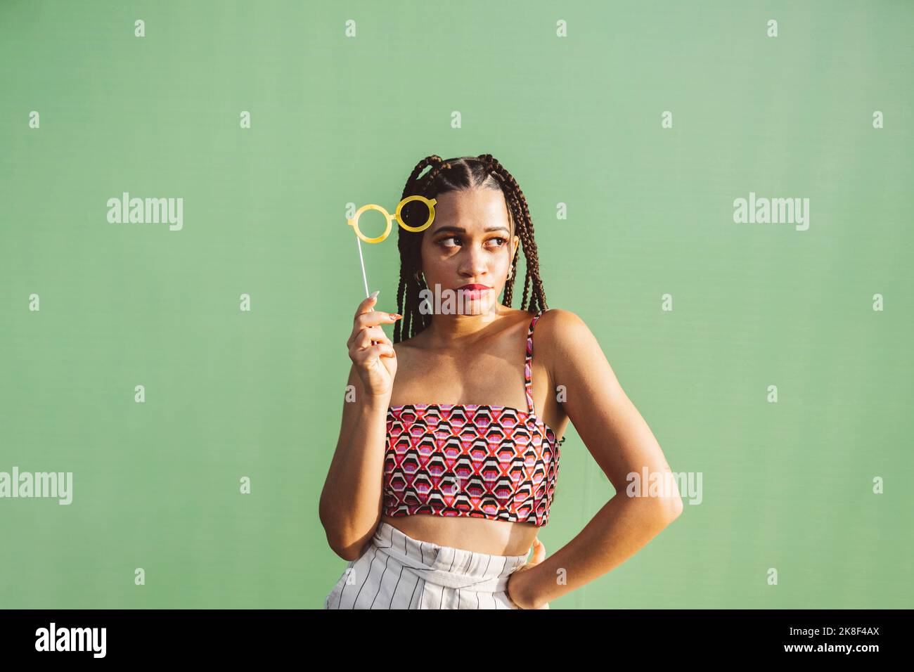 Jeune femme tenant le support de lunettes devant le mur vert Banque D'Images