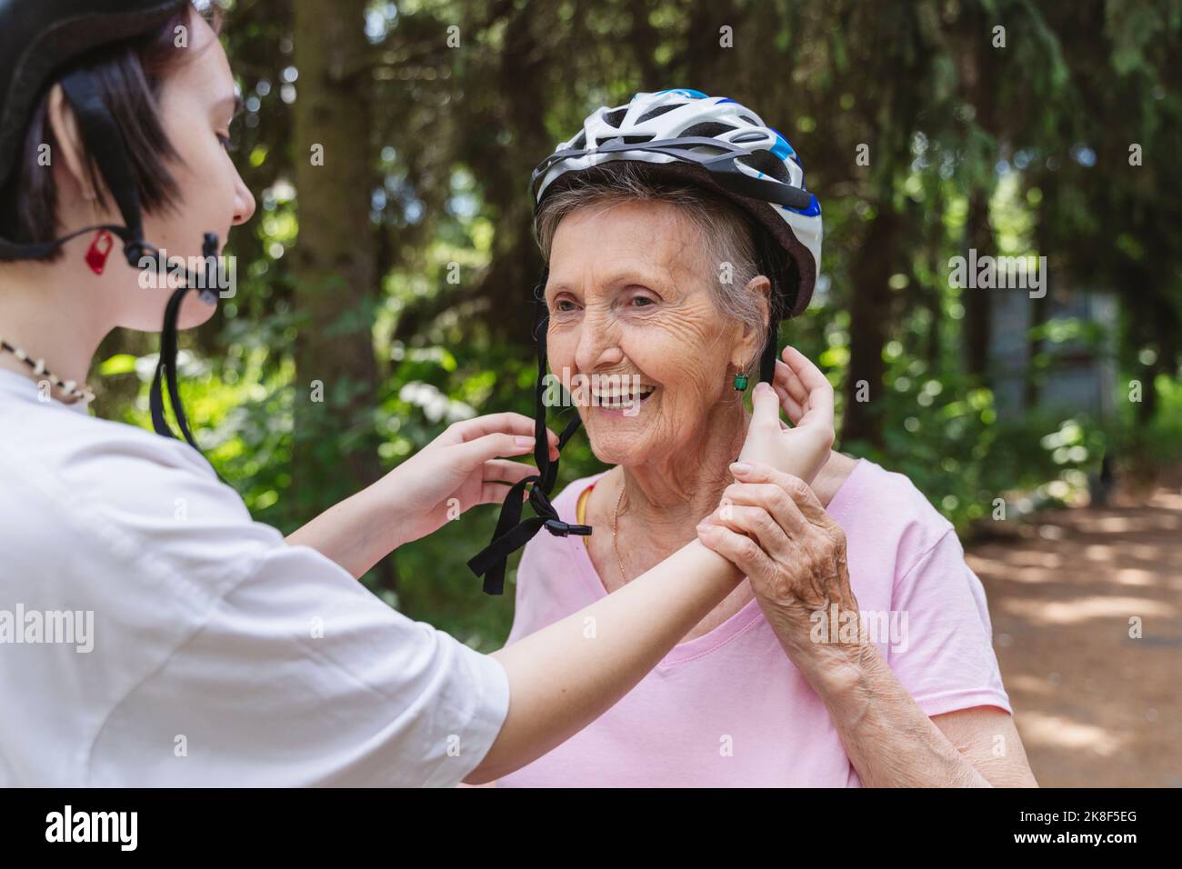 Grande petite-fille aidant une femme âgée portant un casque de vélo dans le parc Banque D'Images