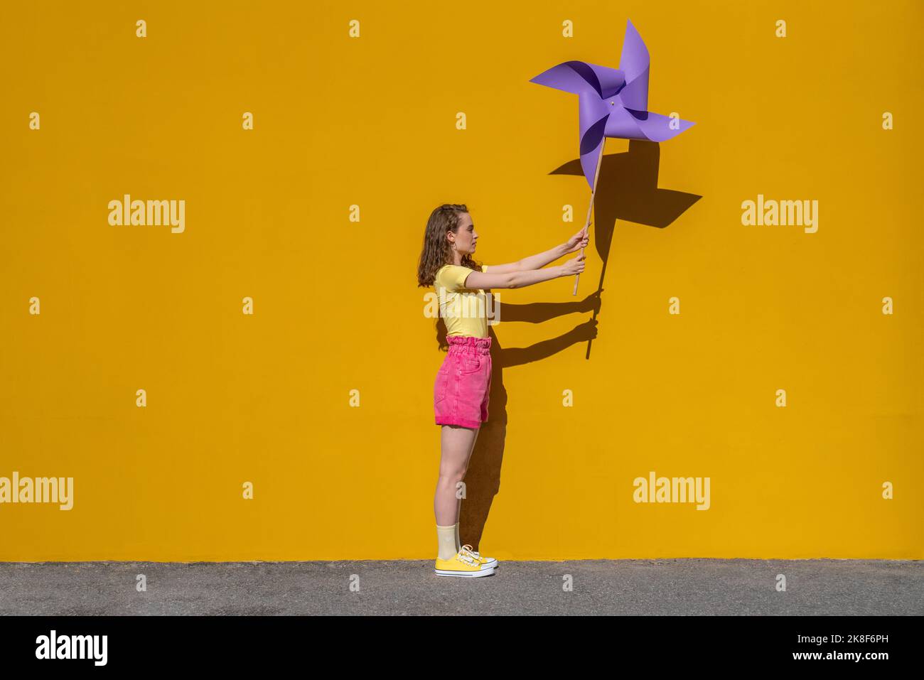 Femme tenant un jouet de roue d'épingle debout devant un mur jaune vif Banque D'Images