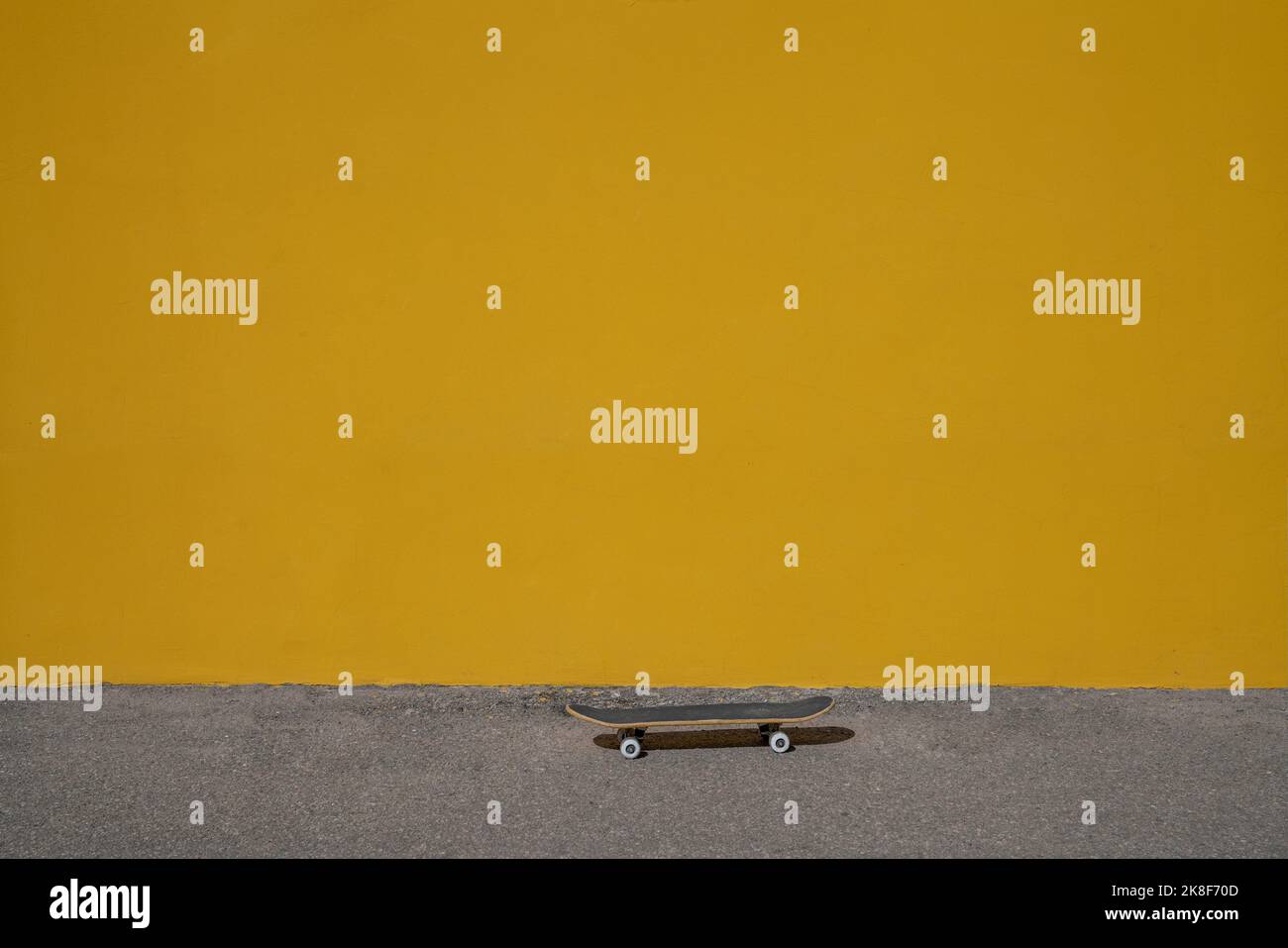 Planche à roulettes sur la piste de marche devant un mur jaune vif Banque D'Images