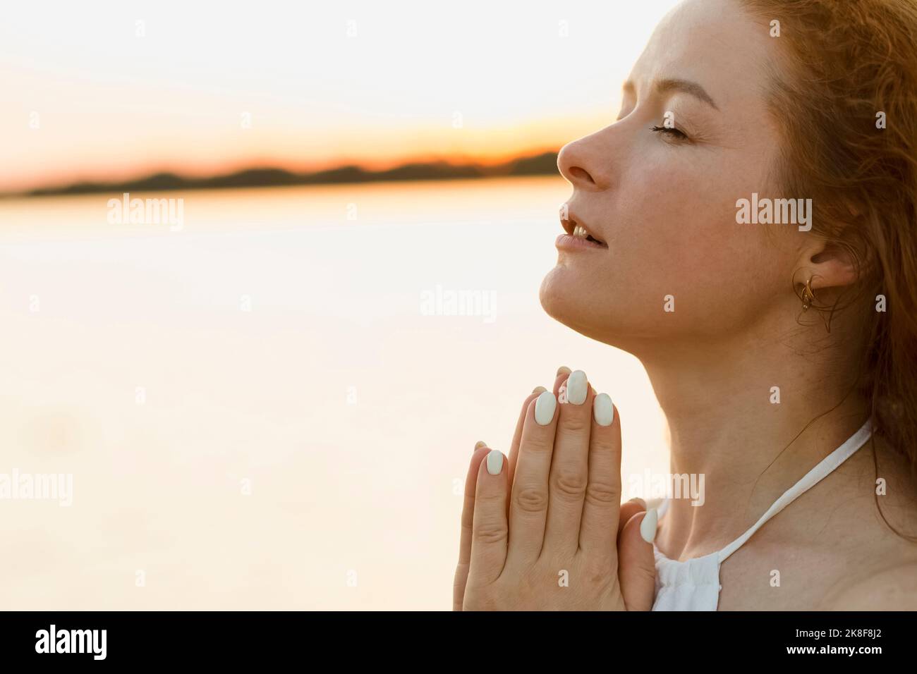 Belle femme aux mains clastées au coucher du soleil Banque D'Images