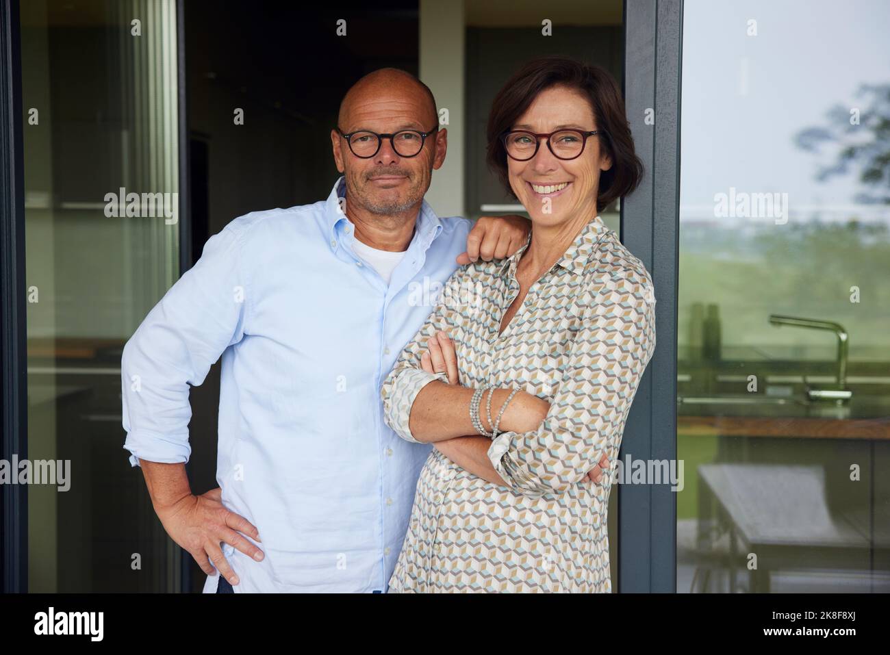 Un couple de personnes âgées heureux se penchant sur une porte en verre Banque D'Images