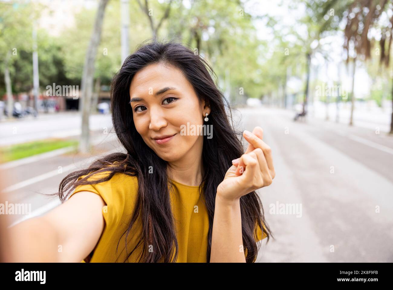 Femme souriante faisant prendre le selfie dans une rue bordée d'arbres dans la ville Banque D'Images