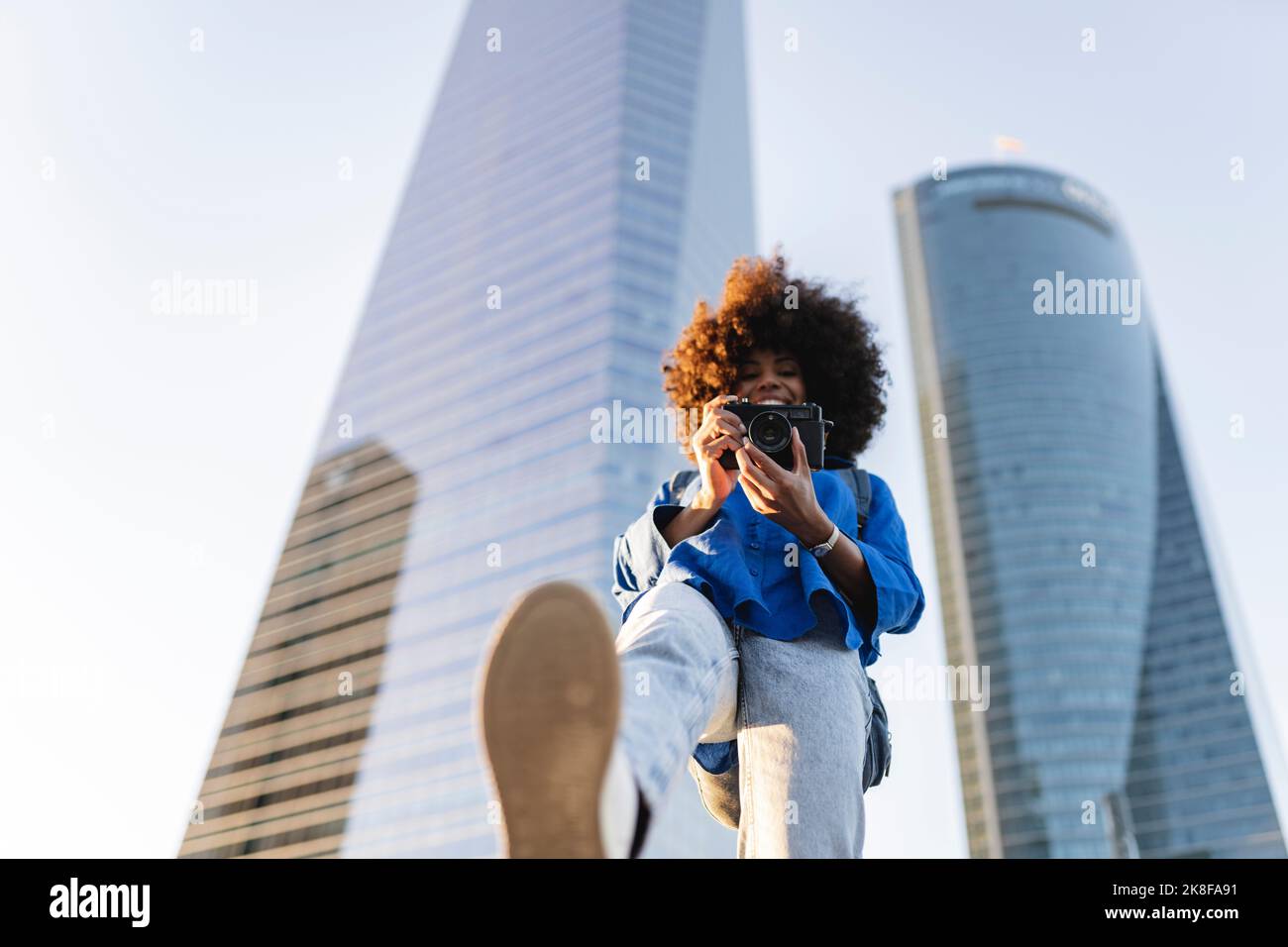 Femme souriante photographiant à travers l'appareil photo devant les bâtiments Banque D'Images