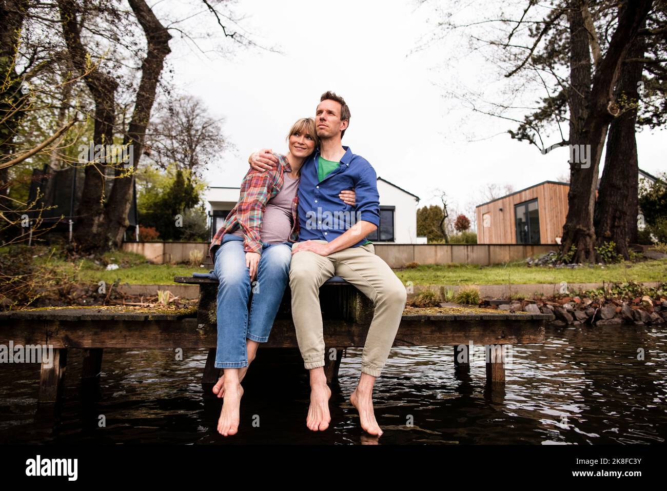 Homme avec le bras autour femme expectant assis sur la jetée au lac Banque D'Images