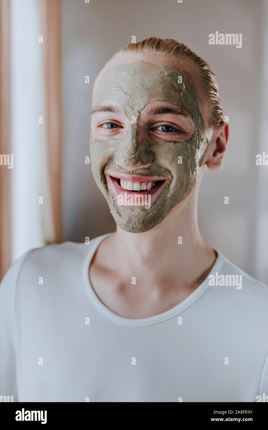Joyeux jeune maquilleur avec masque facial à la maison Banque D'Images