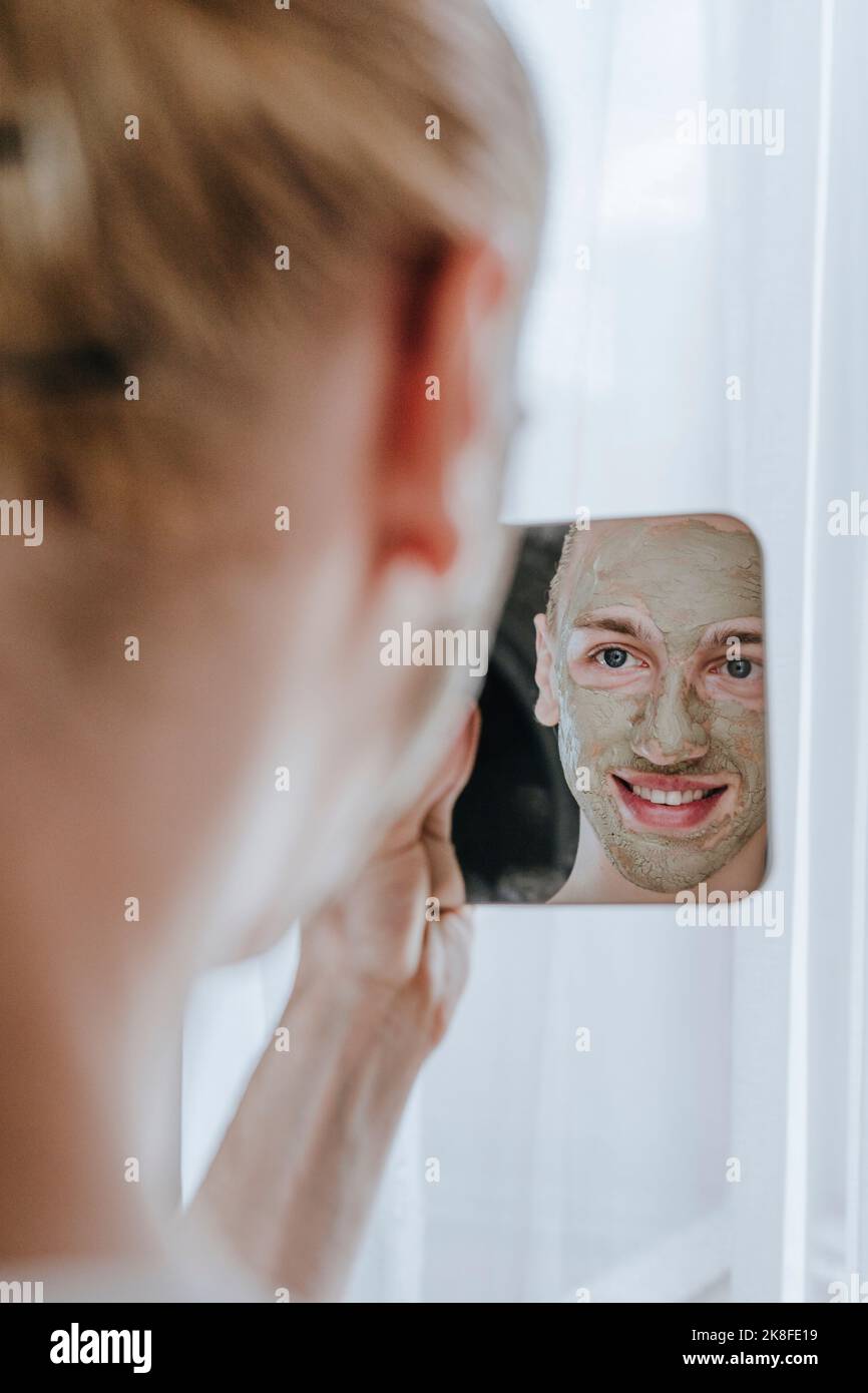 Jeune maquilleur heureux avec masque facial regardant le miroir Banque D'Images